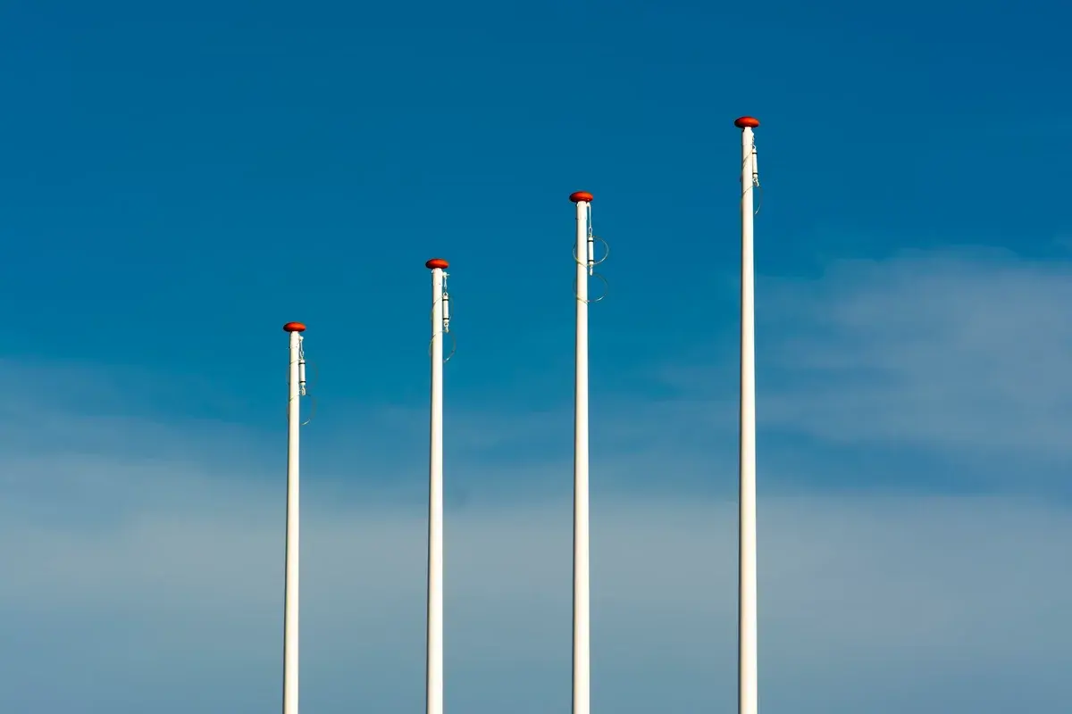 Four tall flagpoles against a blue sky.