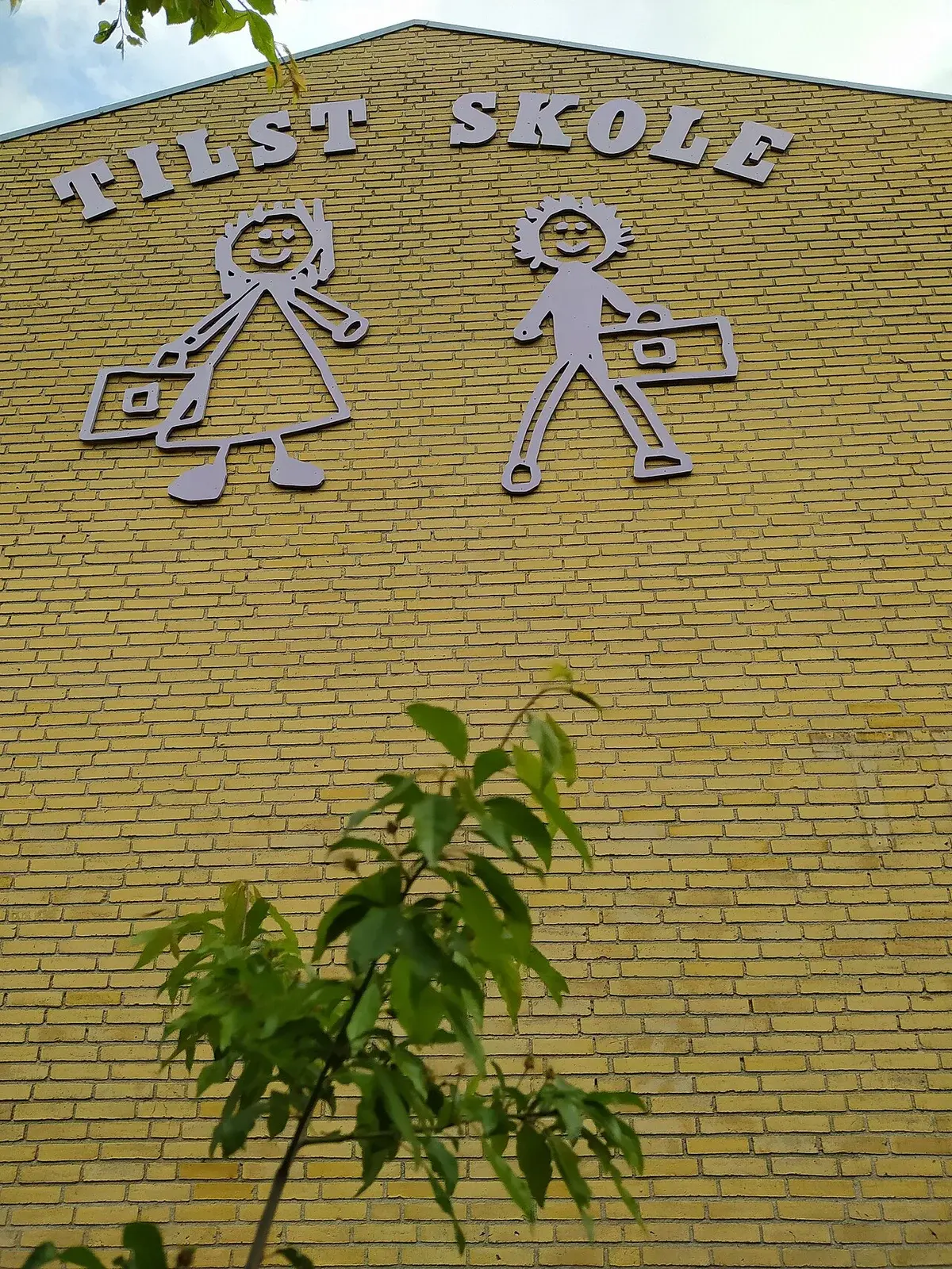 School facade with the name Tilst Skole and two stylized child figures on the wall.