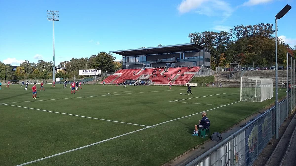 Daytime view of the main grandstand at Harboe Arena during a football match.