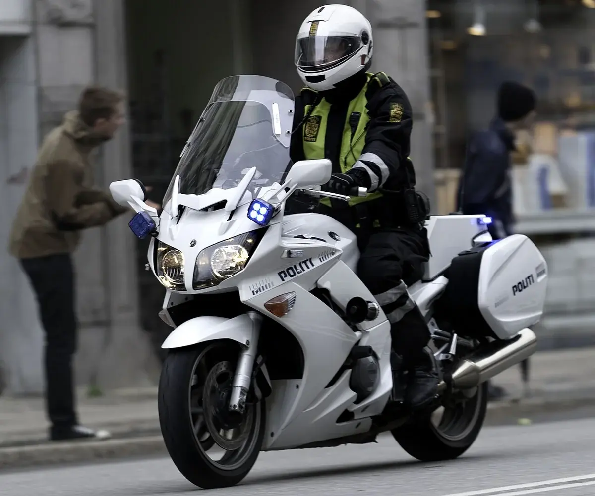 A Danish police officer riding a white police motorcycle with flashing lights in Copenhagen.