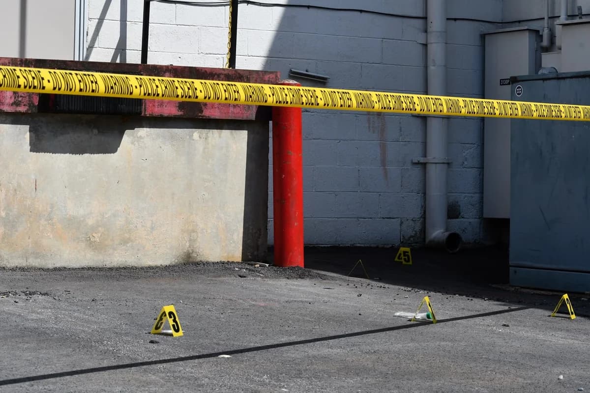 Police tape blocks off an alley with evidence markers on the ground.