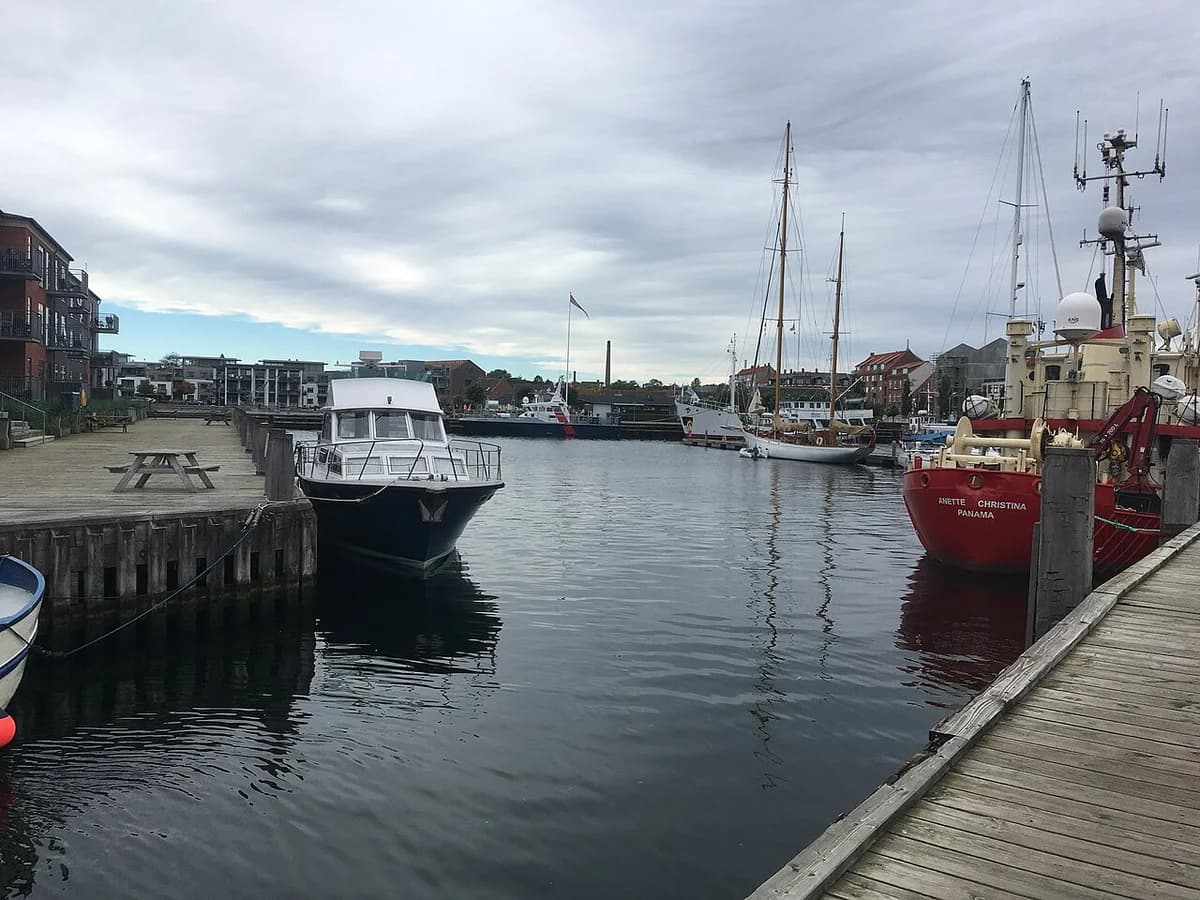 Boats docked at Nyborg harbor with buildings and cloudy sky