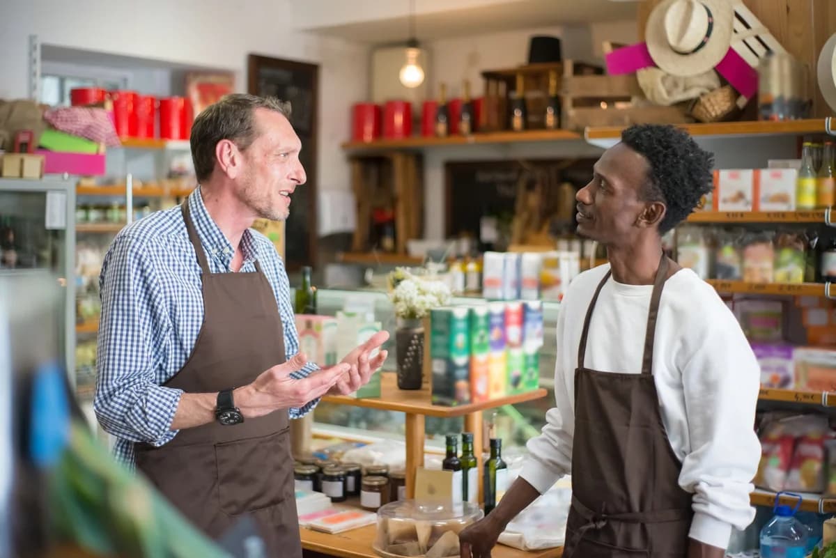 Two grocery store workers in aprons talking