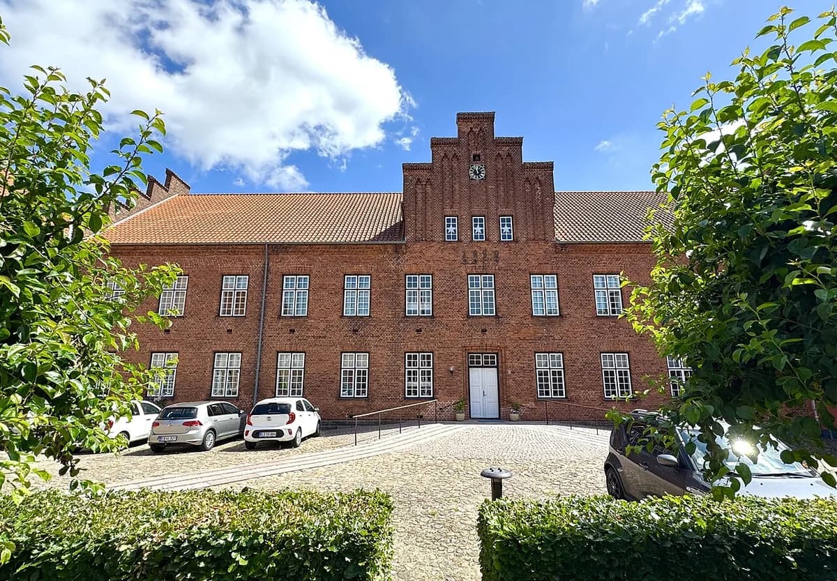 Historic red-brick building with a stepped gable and clock, viewed from a courtyard.