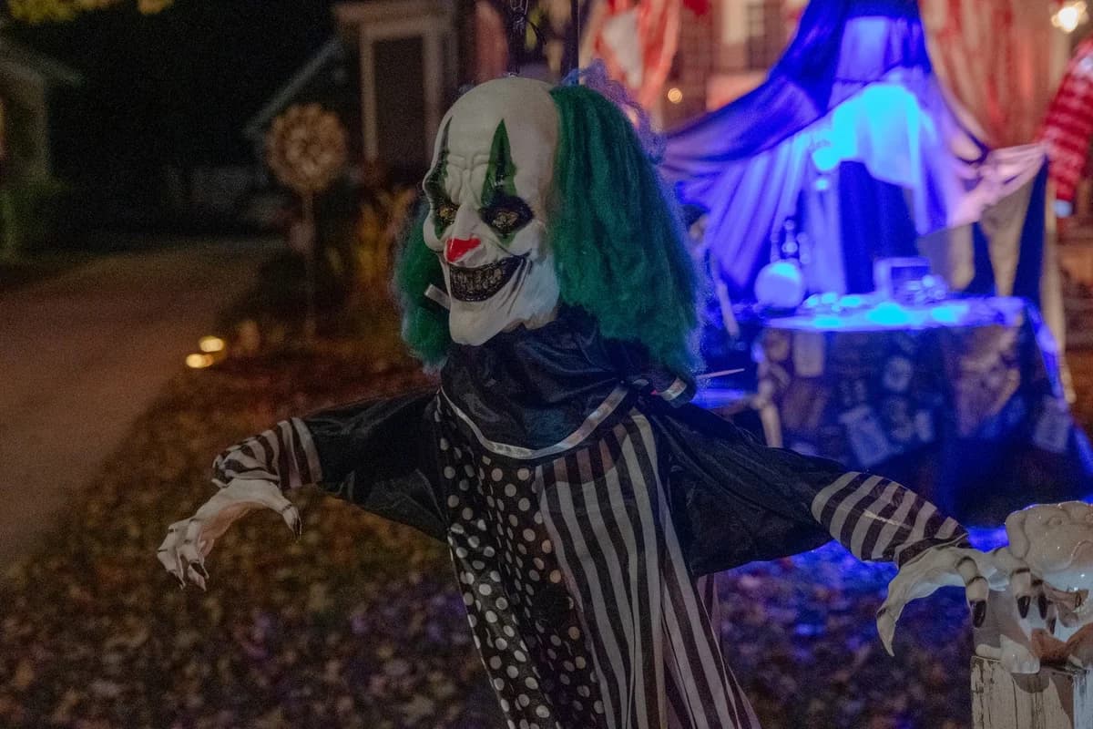 A scary clown decoration lit by colorful Halloween lights.