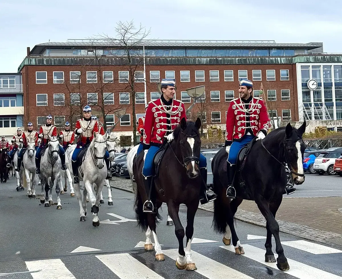 Mounted Guard Hussar Regiment riders in red uniforms riding past a town hall in Slagelse.
