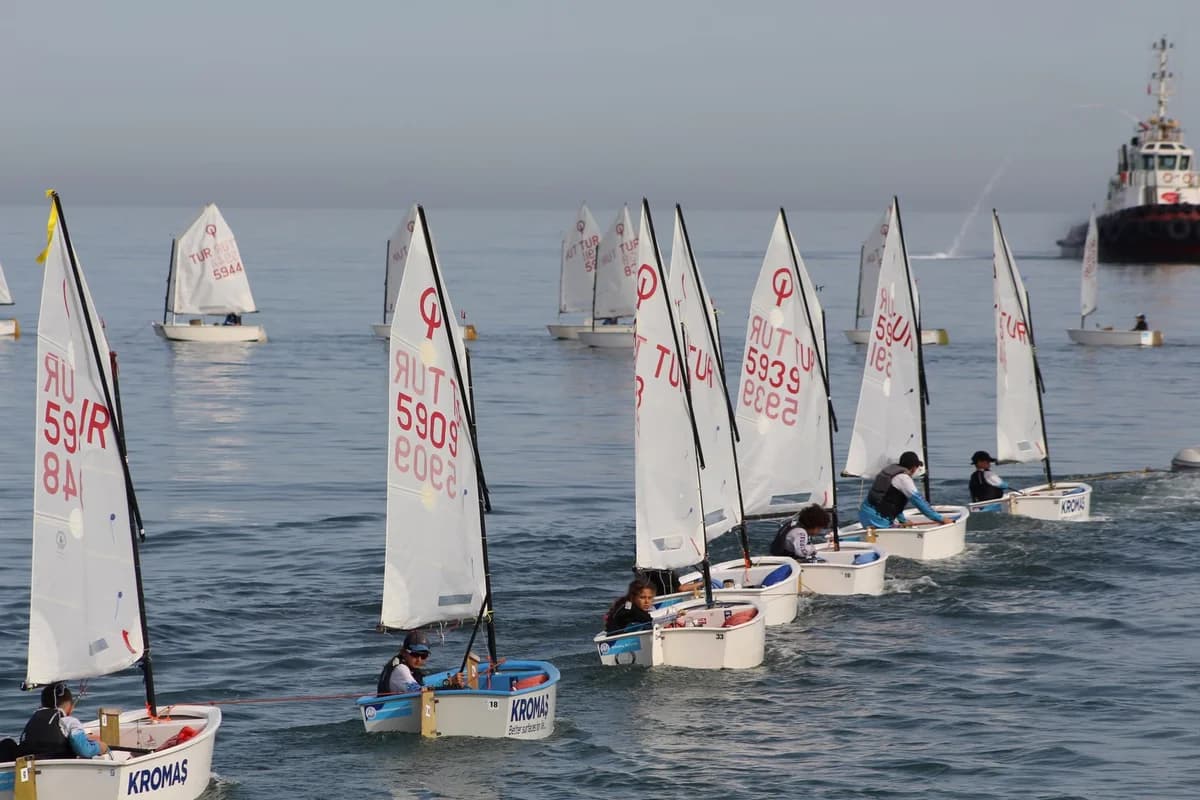 Young sailors racing small sailboats in a regatta on calm water.
