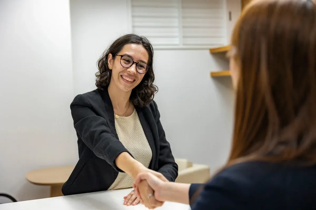 Two women shake hands in an office during a business meeting.