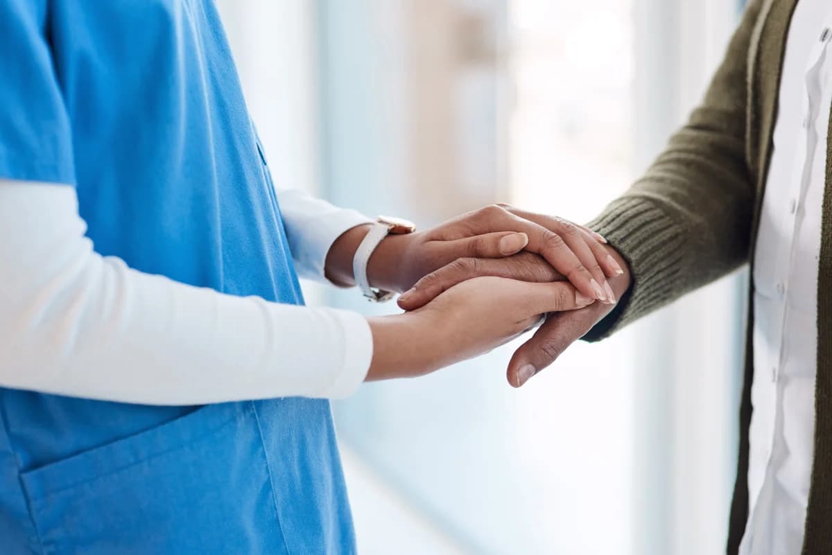 A nurse gently holding hands with an elderly woman.