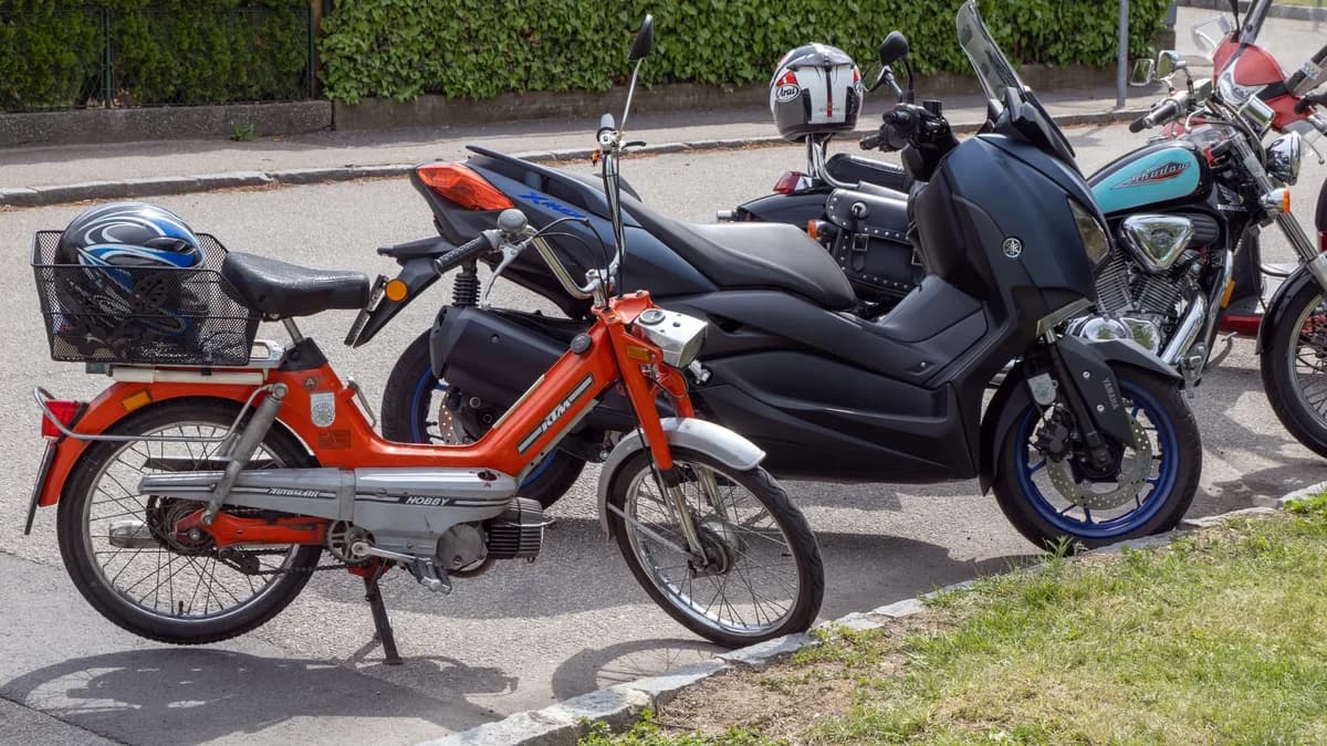 A vintage orange moped parked beside modern motorcycles on a street.