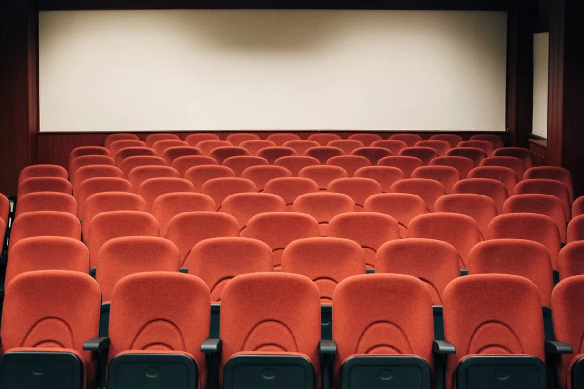 Empty theater with rows of red seats and a blank screen.