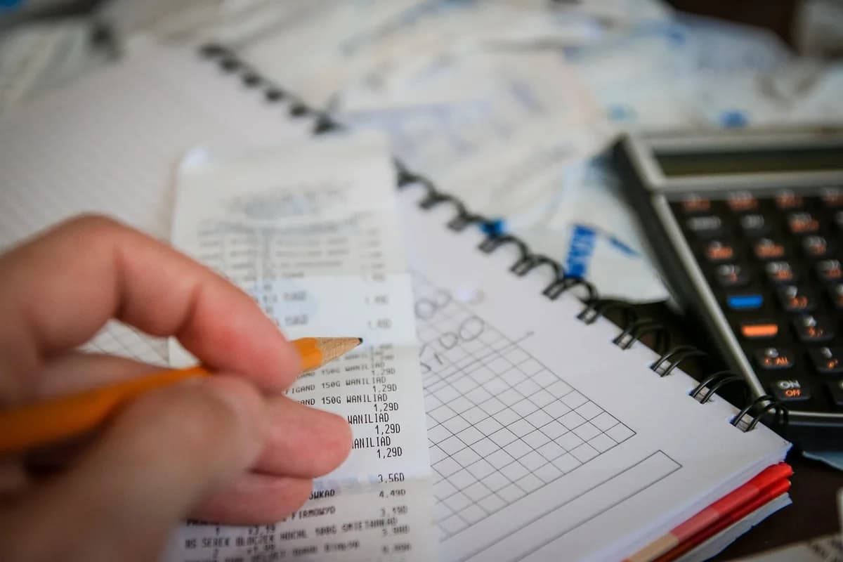 A hand holding a receipt beside a notebook and calculator.
