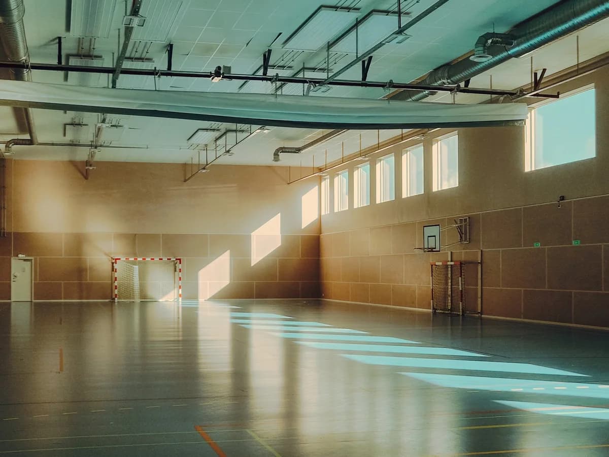 Empty sports hall with sunlight streaming through high windows.