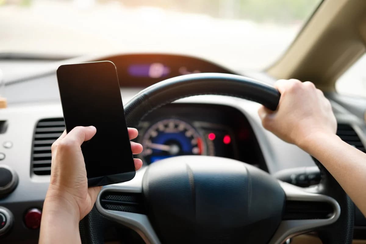 A driver holds a smartphone while steering a car.