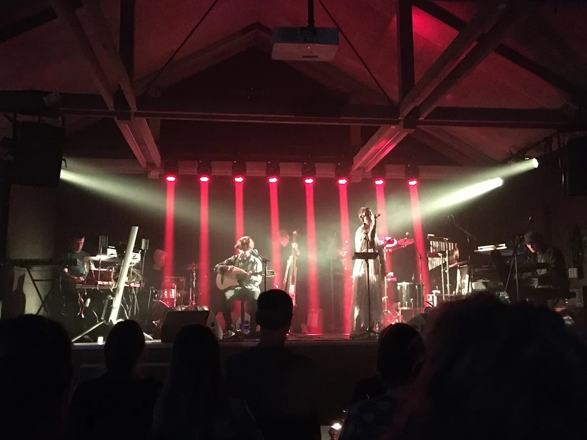 A live band performing on a dimly lit stage with red lights and an audience in front.