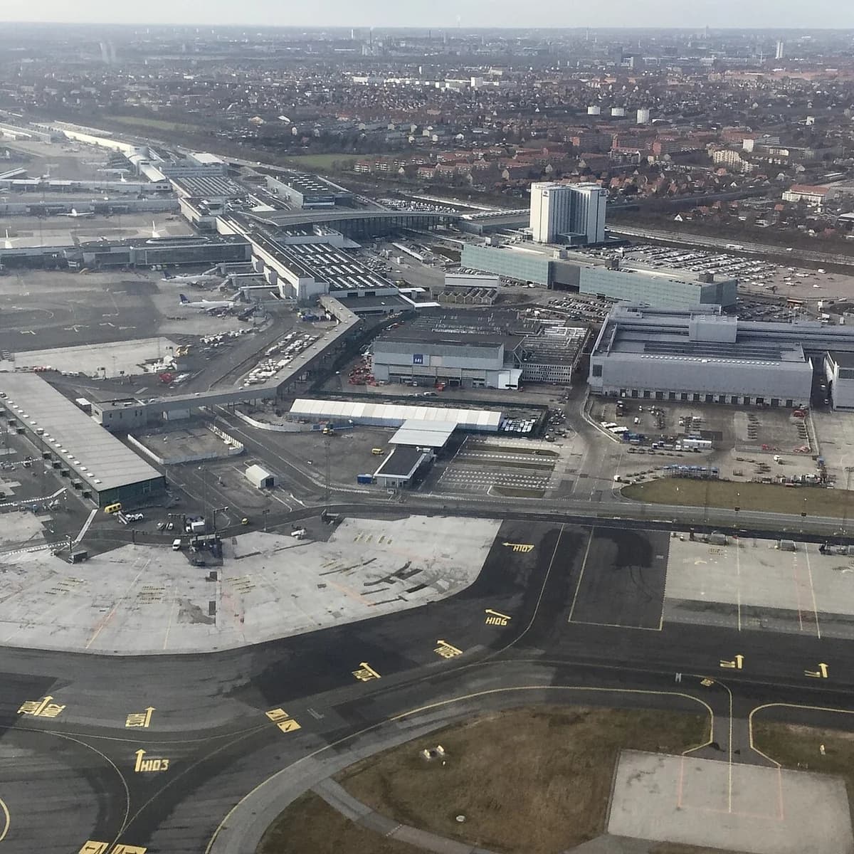 Aerial view of Copenhagen Airport with terminals, taxiways, and the city in the distance.