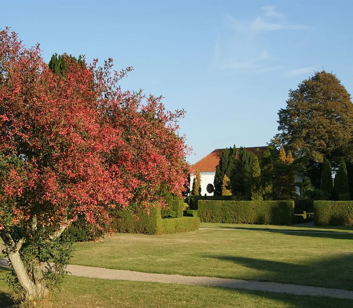 A quiet cemetery with manicured hedges, trees, and a building in the background.