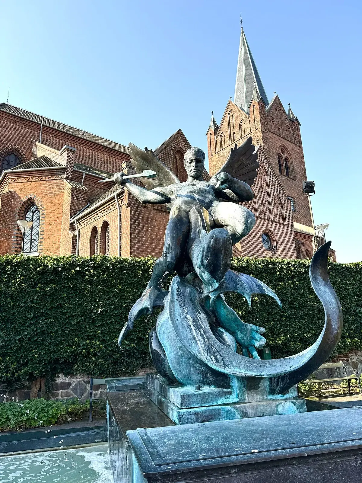 Bronze statue of winged angel fighting dragon by a brick church