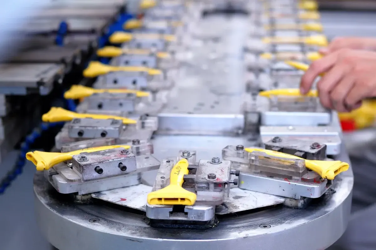 Close-up of yellow components on an industrial assembly line with a worker's hand nearby.