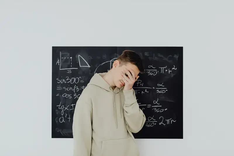 Student covering face in front of blackboard with math formulas