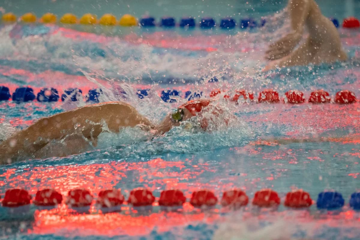 swimmers racing in a pool with colorful reflections